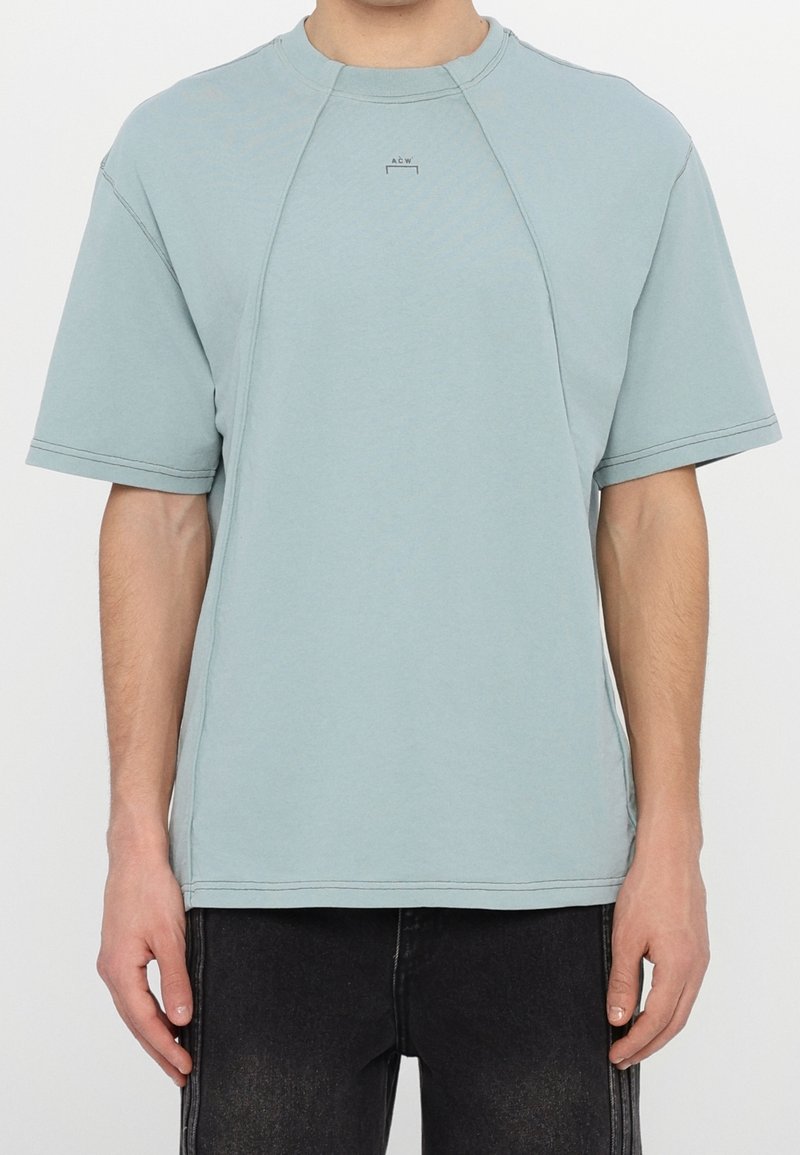 T-shirt bleu clair à manches courtes avec un col rond, des manches raglan, des coutures visibles et un logo subtil sur la poitrine.