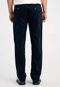 Marineblauwe corduroy broek met verticale ribbelstructuur, twee achterzakken en knoopsluitingen, in een stijl met een vlakke voorkant en taps toelopende pijpen.