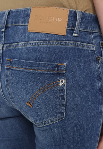 Vaqueros de denim azul con una etiqueta de cuero marrón que dice "DON DUP MADE IN ITALY". Presenta costuras en naranja y un acento metálico en el bolsillo trasero.