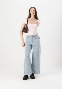 Vaaleanpunainen ribbitoppi, jossa on lyhyet hihat, korkeavyötäröiset vaaleansiniset leveälahkeiset farkut, mustat paksupohjaiset kengät ja pieni tumma käsilaukku.