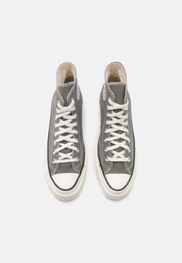 Wysokie sneakersy z szarego materiału z białymi sznurówkami, białą czubką i czarnym wykończeniem. Posiadają okrągłe logo po boku.