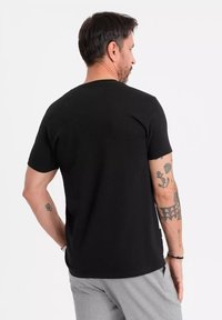 T-shirt noir à manches courtes en coton, avec un col rond classique et une texture lisse ; porté de manière visible de dos.