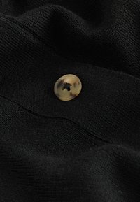 Țesătură neagră cu o suprafață texturată, având un nasture rotund, marmorat, cu un design cu patru găuri, poziționat central pe material.