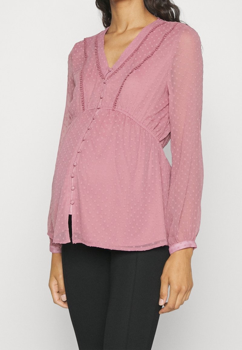 Blouse rose texturée avec manches longues bouffantes, encolure en V, fermeture à boutons sur le devant et détails froncés à la taille.