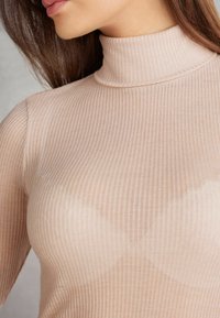 Jasnobeżowy prążkowany golf o dopasowanym kroju, z wysokim kołnierzem i miękką teksturą, podkreślający pionowe paski.