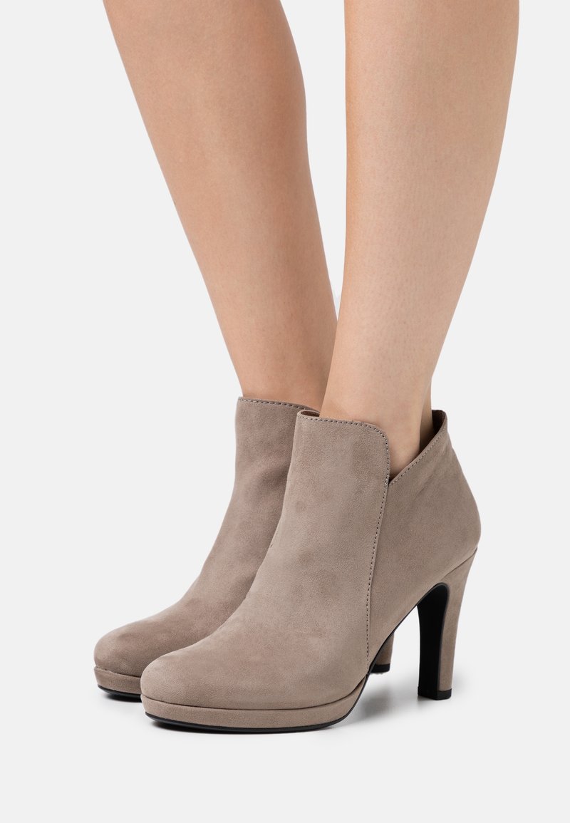 Bottines beiges en daim avec bouts arrondis et talons carrés hauts, portées pieds nus sur un fond uni.