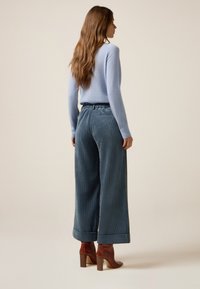 Hellblauer Pullover mit langen Ärmeln, kombiniert mit dunkelblauen Cordhosen mit weitem Bein und breitem Bund. Braune Absatzstiefel.