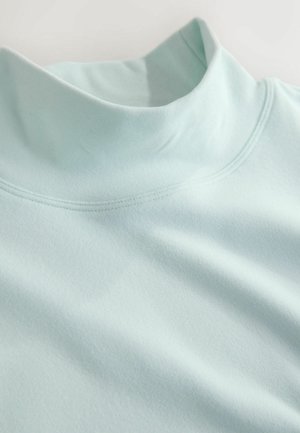 Lyseblå højhalset skjorte lavet af blødt stof. Har en glat tekstur med kontrastsyning langs halsudskæringen og skuldrene.