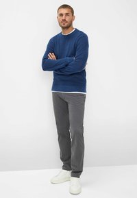 Blauwe gebreide crewneck trui gedragen met grijze chino's en witte sneakers. De trui heeft ribgebreide manchetten en een onderrand. Eenvoudig ontwerp, geen patronen.