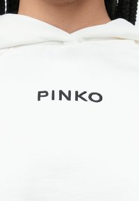 Balta kapuce ar mīkstu tekstūru un priekšējām kabatām. Uz krūšu zonas centrā atrodas melns izšūts uzraksts "PINKO".