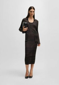 Mustat ruudulliset neulemekko yhdessä sopivan pitkähihaisen neuletakin kanssa, jossa on V-pääntie, pitkät hihat ja nappikoristeet; yhdistetty mustiin korkokenkiin.