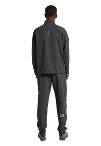 Dunkelgraue Outdoor-Jacke mit hohem Kragen und Rückenschriftzug "ATW", kombiniert mit passenden Cargo-Hosen mit Seitentaschen und der Nummer "223".