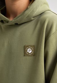 Felpa verde oliva con una texture morbida, caratterizzata da una piccola patch quadrata con il testo "Petrol Industries" e una "P" stilizzata.