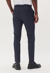 Marinblå rutiga byxor med slim fit, utrustade med två bakfickor och knappstängning. Materialet ser slätt ut med subtila texturdetaljer.