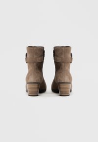 Bottines en daim marron avec un talon empilé. Dotées d'une sangle avec une boucle en métal. Texture lisse et design épuré et simple.