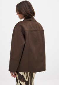 Rjava nubuk oversized jakna s ovratnikom, ki ima strukturirano hrbtno stran in spuščena ramena, v kombinaciji z vzorčenim spodnjim delom.