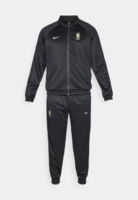 Črn Nike trenirni komplet z jakno na zadrgo in ovratnikom, elastičnimi manšetami ter usklajenimi hlacami z žepi. Vključene so tudi nalepke z NBA logotipom.