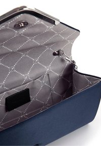Navyblaue Handtasche mit strukturiertem Design, ausgestattet mit einem grauen gemusterten Innenfutter, einem Druckverschluss und einer Innentasche mit Etikett.