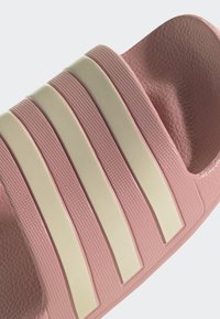 Ružové šľapky s tromi širokými krémovými pruhmi. Vrchná časť má textúru a stielka je tvarovaná pre pohodlie. Vyrobené z odolného syntetického materiálu.