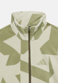 Ζακέτα φλις με φερμουάρ σε ανοιχτό πράσινο και κρεμ, με γεωμετρικά σχέδια, ψηλό γιακά και διακριτικό λογότυπο στο στήθος.