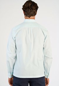 Lichtblauw overhemd met lange mouwen en een button-down kraag, met een plooi aan de achterkant en knoopaccenten op de manchetten. Glad oppervlak.