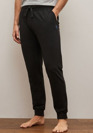 Pantalones de chándal negros hechos de una tela suave con cintura elástica y cordón, piernas ajustadas y un pequeño logo azul en la cadera izquierda.