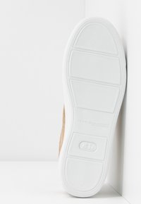 Semelle d'une chaussure beige avec une semelle extérieure en caoutchouc blanc, comportant des panneaux de grip texturés et un détail de marque embossé au centre.