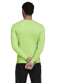 Neon groene langekous prestatieshirt met een ronde hals, smalle pasvorm en een zachte textuur, weergegeven van de achterkant. Zwarte broek complementeren het shirt.