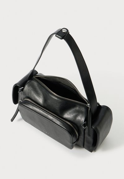 Borsa in pelle nera con una forma strutturata, dotata di più scomparti con zip, una lunga tracolla regolabile e un logo inciso in modo discreto.
