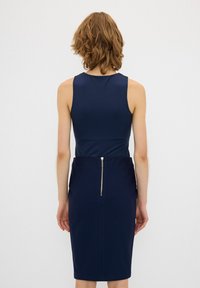 Abito aderente blu navy con design senza maniche, caratterizzato da una cerniera sul retro e un tessuto morbido e elastico. La silhouette sagomata enfatizza la forma.