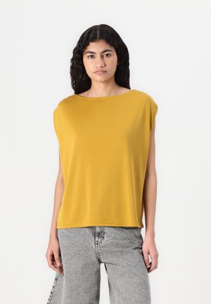 Mosterdgele, losse korte mouw top met een brede bootnek. Zachte stof met een gladde textuur, gecombineerd met grijze geprinte jeans.