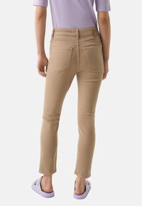 Beige fitted jeans with a mid-rise waist, five pockets, and a button closure. The fabric appears smooth with a slight stretch.