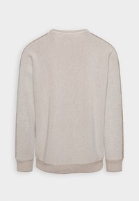 Beige striktrøje med ribbet struktur, lange ærmer og rund halsudskæring. Har subtil tonale detaljer langs skuldersømmen.