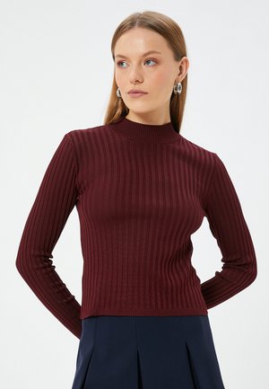 Burgundy ribbed long-sleeve sweater with a high neck. Features a fitted design and textured fabric, paired with a dark skirt.