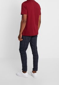 Camiseta corta de manga en color burdeos combinada con pantalones de cuadros azul marino, con un corte ajustado y zapatillas blancas. Material visible de mezcla de algodón.