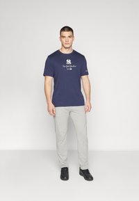 Granatowa koszulka z białym logo "New York Yankees", zestawiona z jasnoszarymi spodniami. Całość uzupełniają czarne trampki.