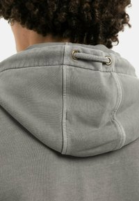 Gray sweatshirt hood with a braided drawstring and gold-tone eyelets. Soft texture and visible stitching detail on the neck area.