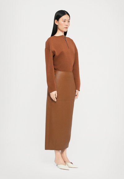 Rjav zip-up pulover s krožnim izrezom, v kombinaciji z dolgo rjavo usnjeno krilom. Bele pointed flats čevlje dopolnjujejo videz.