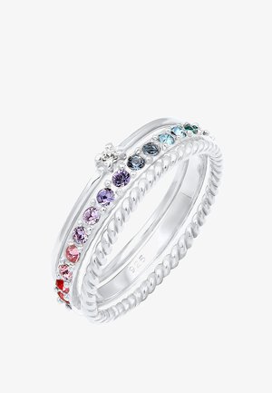 Trois bagues en argent sterling empilées, une avec des pierres précieuses multicolores, une avec une pierre claire unique, et une avec un motif torsadé en forme de corde.