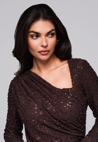 Braunes Paillettenoberteil mit drapiertem Design, einem quadratischen Ausschnitt und strukturierten Akzenten. Lange Ärmel mit Manschetten zeigen filigrane Verzierungen.