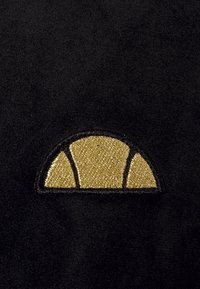 Svart tyg med en guldbroderad halvcirkel design med strukturella detaljer, mot en jämn bakgrund.