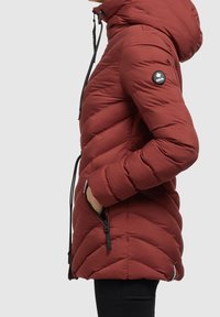 Chaqueta de plumas roja con capucha, acolchado en forma de flecha, bolsillos laterales con cremallera y un parche con el logo en la parte superior del brazo. Cuenta con puños elásticos y dobladillo ajustable.