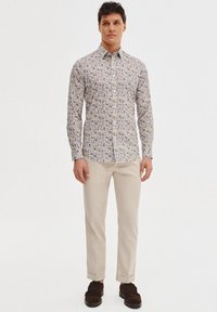 Wzorzysta koszula z guzikami w kolorze białym z wielokolorowym motywem kwiatowym. Slim fit i z bawełny. Połączona z beżowymi spodniami i ciemnymi butami.