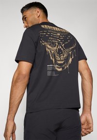 Sort kortærmet t-shirt med et stort guldkraniumgrafik på ryggen, inklusive tekst og en glat bomuldsfølelse. Enkel crew neck-design.
