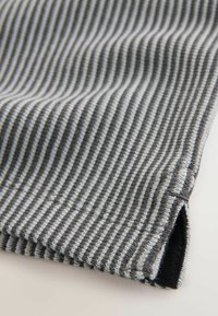 Grau-weißer gestreifter Stoff mit glatter Textur, am Rand gefaltet, mit einem schwarzen Akzent an der Naht.