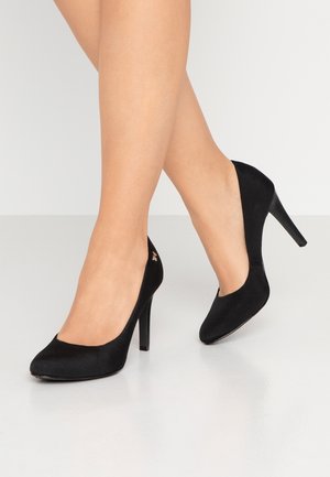 Zapatos de tacón alto de ante negro con puntera redondeada y silueta elegante. Presentan un tacón de aguja puntiagudo y un pequeño detalle metálico con el logo.