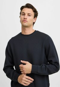 Zwarte crewneck sweatshirt van zacht materiaal, met ribbelmanchetten en -zoom, en zichtbare stikdetails op de halslijn en mouwen.