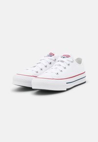 Zapatillas de lona blancas con punta redonda, suela de goma, acentos rojos y azules, y diseño clásico de cordones; presenta un logo de estrella en la lengüeta.