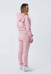 Felpa con cappuccio rosa e joggers coordinati in un tessuto morbido. Presenta polsini a costine, una vestibilità comoda e sneakers sportive bianche.