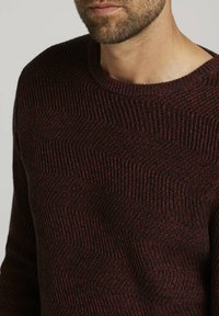 Gestrickter Pullover in Dunkelrot und Schwarz, mit einem strukturierten Zickzackmuster. Rundhalsausschnitt und gerippte Bündchen sorgen für zusätzliches Detail.